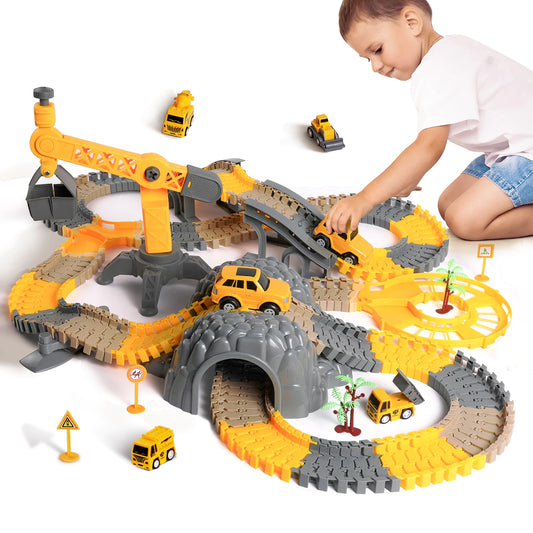 Smiling child playing with a large construction-themed toy car track set. The track features winding roads, bridges, a tunnel, and a rotating crane, all in yellow, gray, and orange colors. Several small construction vehicles, including trucks, excavators, and jeeps, are placed on the track along with road signs and palm tree decorations, creating a realistic construction play environment.