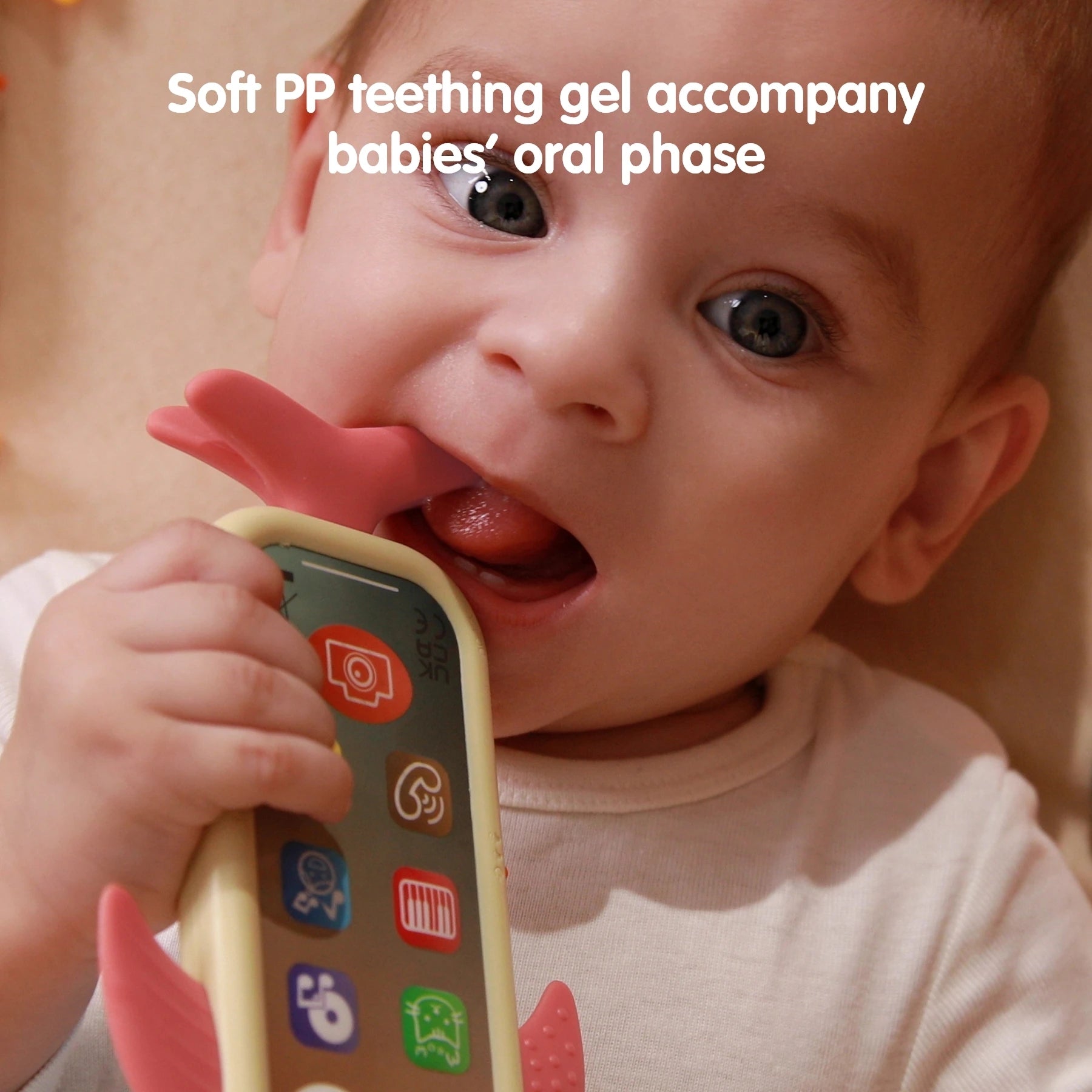 A baby chewing on the pink tail of a whale-shaped baby toy phone with colorful app icons on the screen. Text at the top reads “Soft PP teething gel accompany babies’ oral phase.”