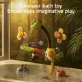 A playful dinosaur-themed bath toy is attached to the side of a bathtub. Water sprays from the dinosaur's mouth onto a colorful spiral track, with floating submarine and narwhal toys nearby. Flower-shaped suction cup toys with bee and ladybug designs are also attached to the tub. The scene is warmly lit, and the text reads 