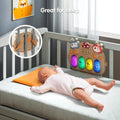 Baby lying in crib with colorful musical keyboard toy attached to the crib rails, glowing lights on piano keys, inset showing back straps for secure attachment.