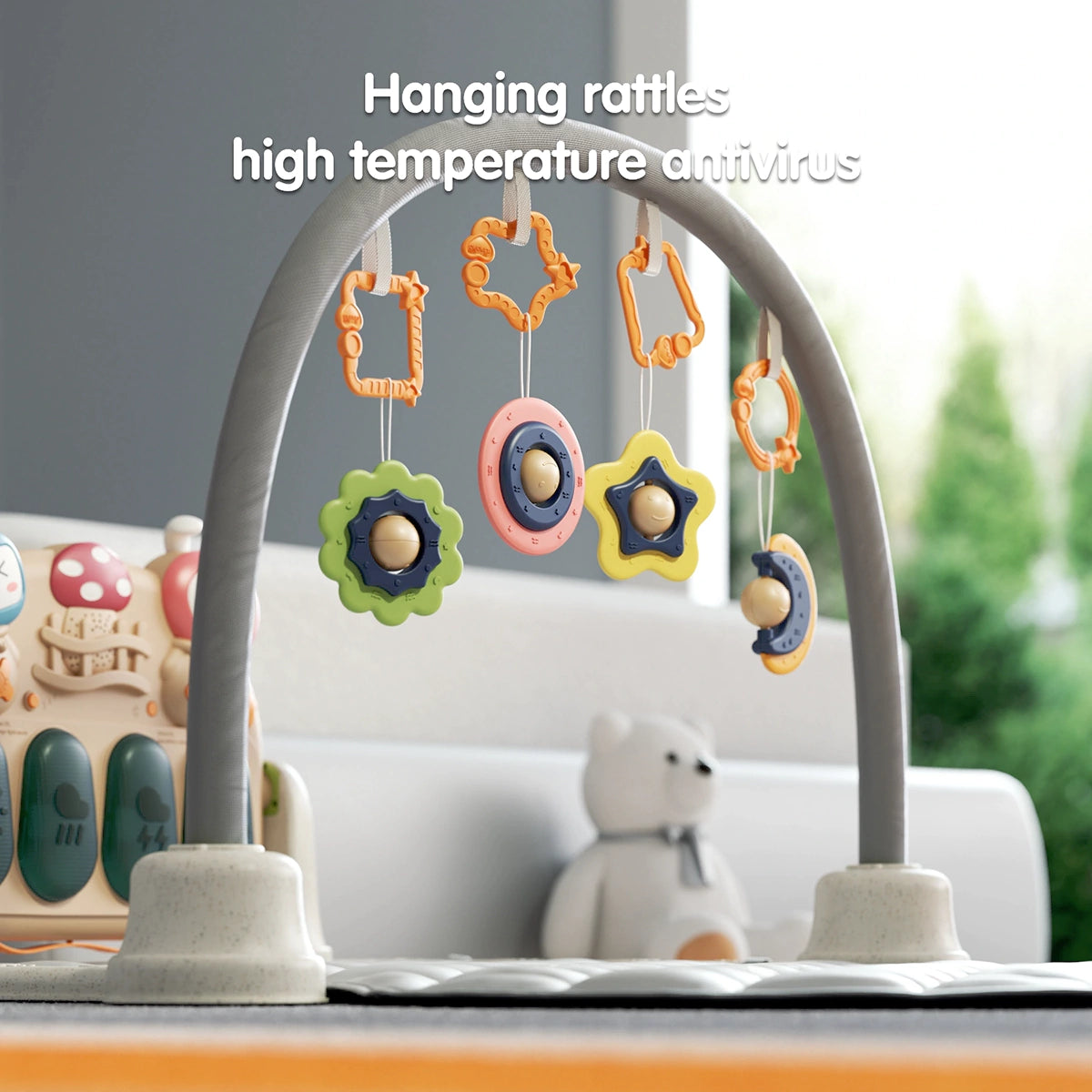 Close-up of baby gym arch with colorful hanging rattles in star, flower, ring, and moon shapes, made of chewable material, high temperature resistant; musical keyboard unit visible in background.