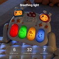 Close-up of a baby gym keyboard panel with four illuminated breathing light keys in red, green, yellow, and blue, each with weather and moon icons. Two cartoon face figures sit on top of the panel, and text highlights 6 LED light sources, 32 lighting effects, and 7 natural colors.